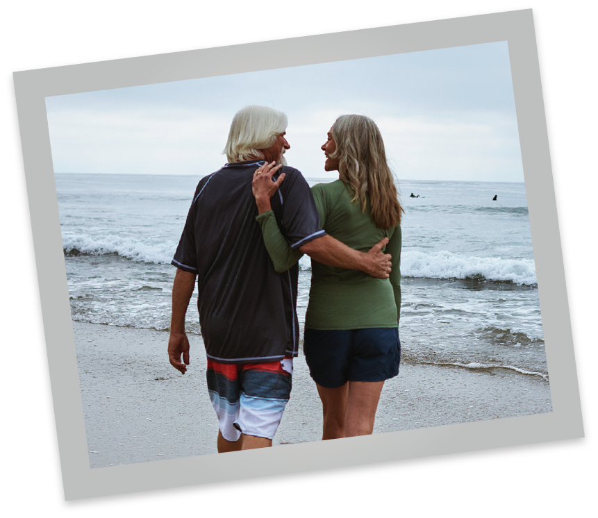 The backside of a couple with arms around each other at the beach